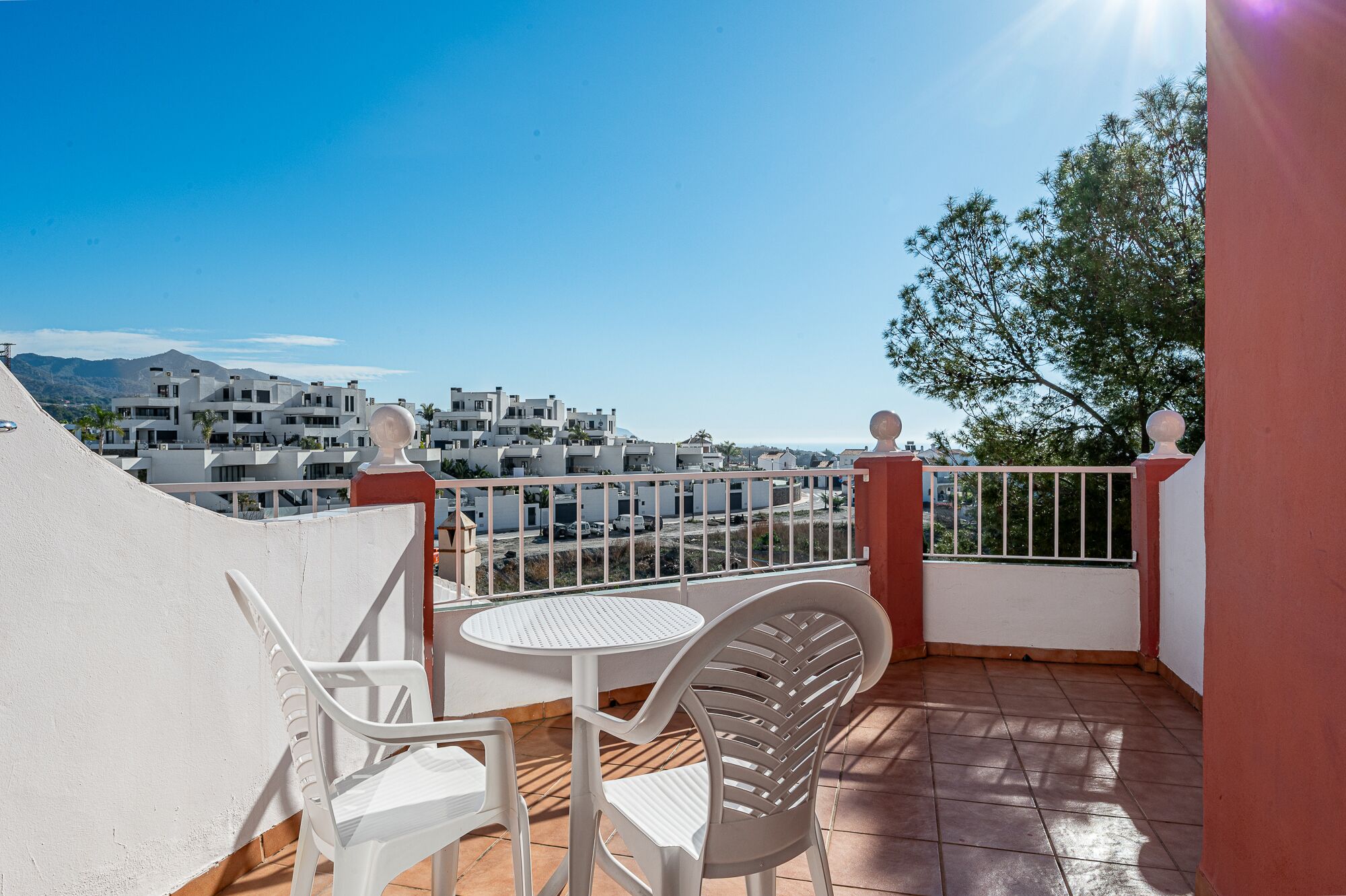 Un balcón con mesa y sillas, con vistas a una zona residencial con edificios modernos y cielo despejado.
