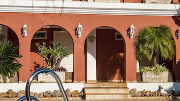A poolside area with a metal ladder, a red building with arched doorways, and potted plants.
