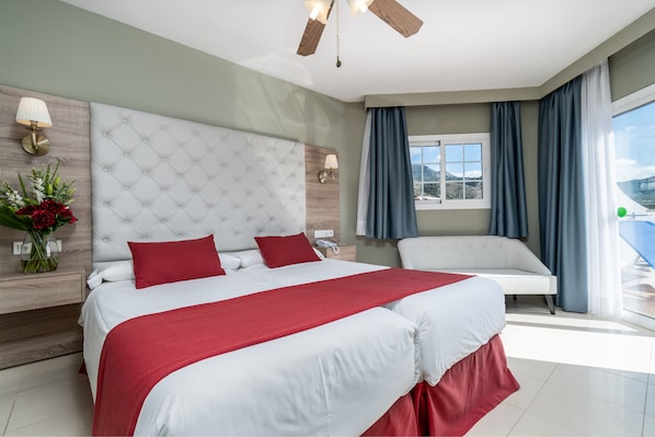A modern hotel room with a large bed, a sofa, a window with curtains, and a view of the outdoors. - Hotel Los Arcos (Nerja)