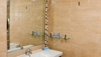 A bathroom with a white sink, mirror, and toilet. There are towels on the sink and a trash can next to the toilet.