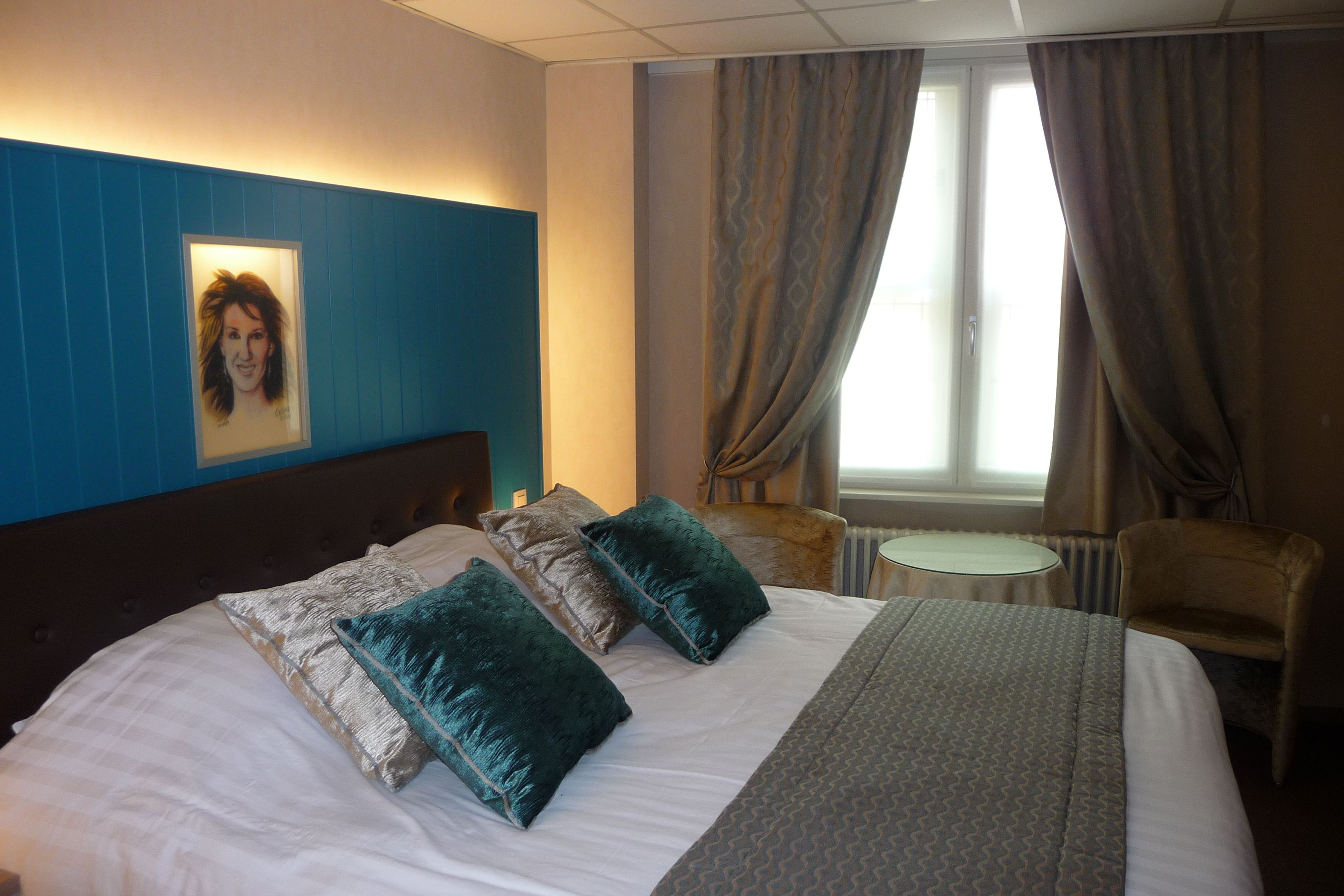 Ein Hotelzimmer mit Bett, zwei Kissen, einem Sessel, einem kleinen Tisch und einem Fenster mit Vorhängen.