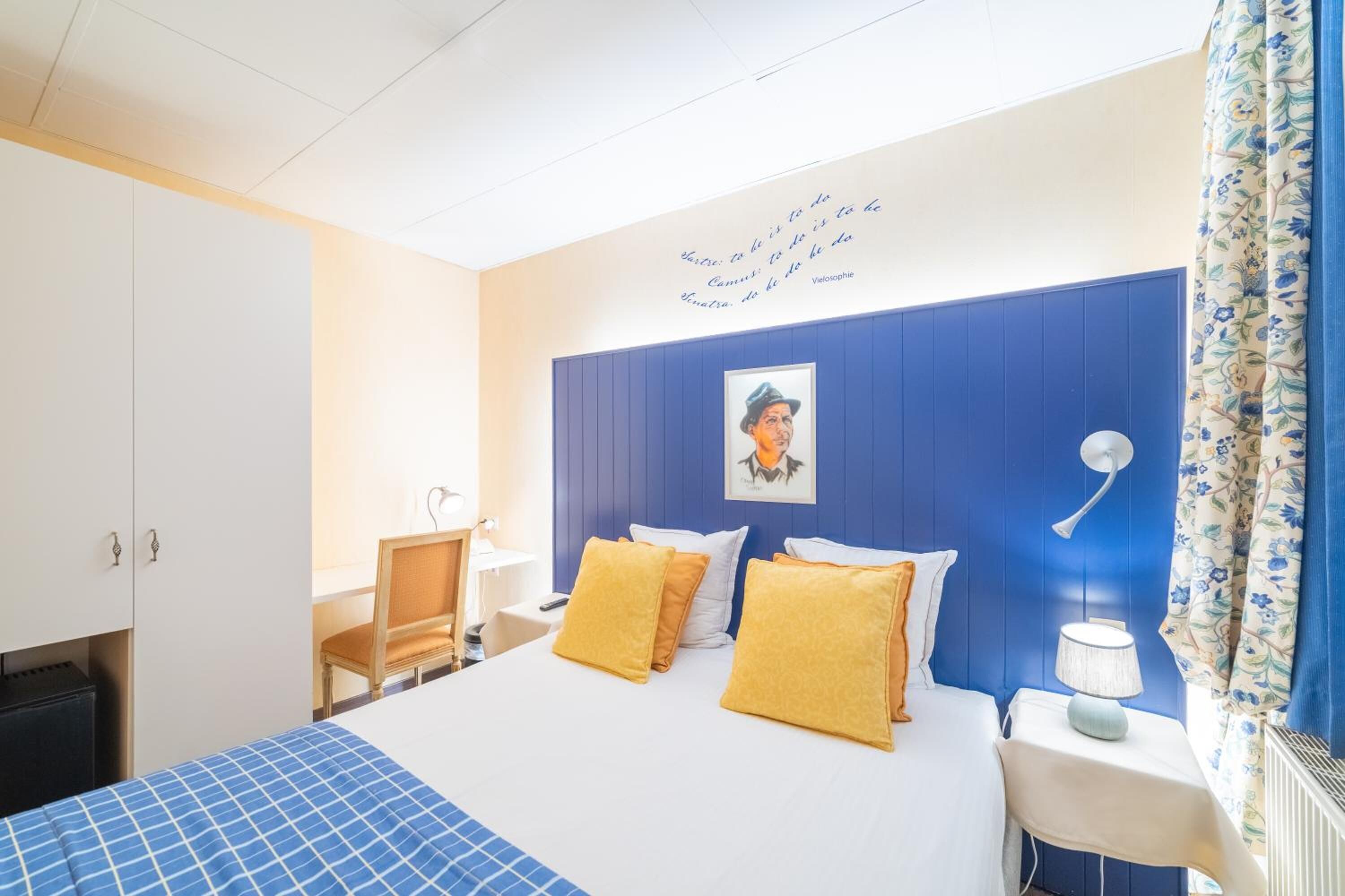 Una habitación de hotel con una cama, un escritorio, una silla, una lámpara y una pared con una cita.