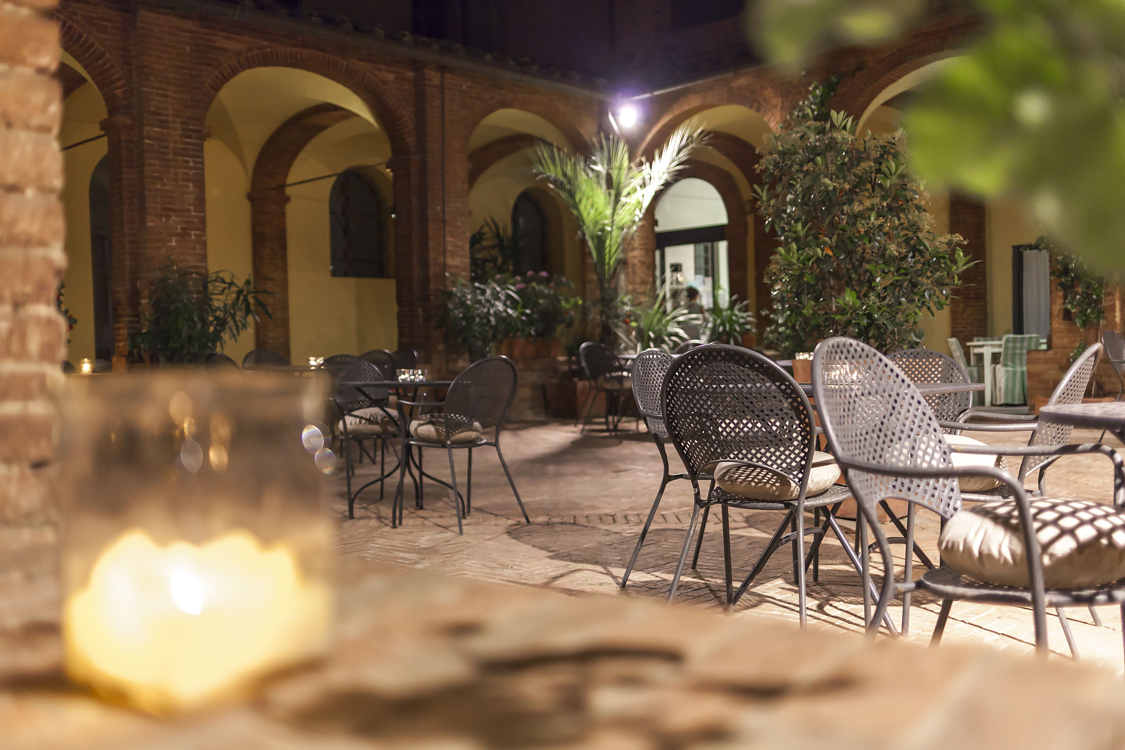 An outdoor patio with brick arches, metal chairs, and potted plants.