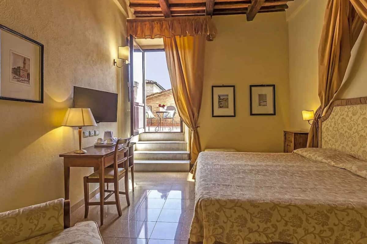 Habitación de hotel con dos camas, un escritorio con silla, televisor y una escalera que da a un área exterior.