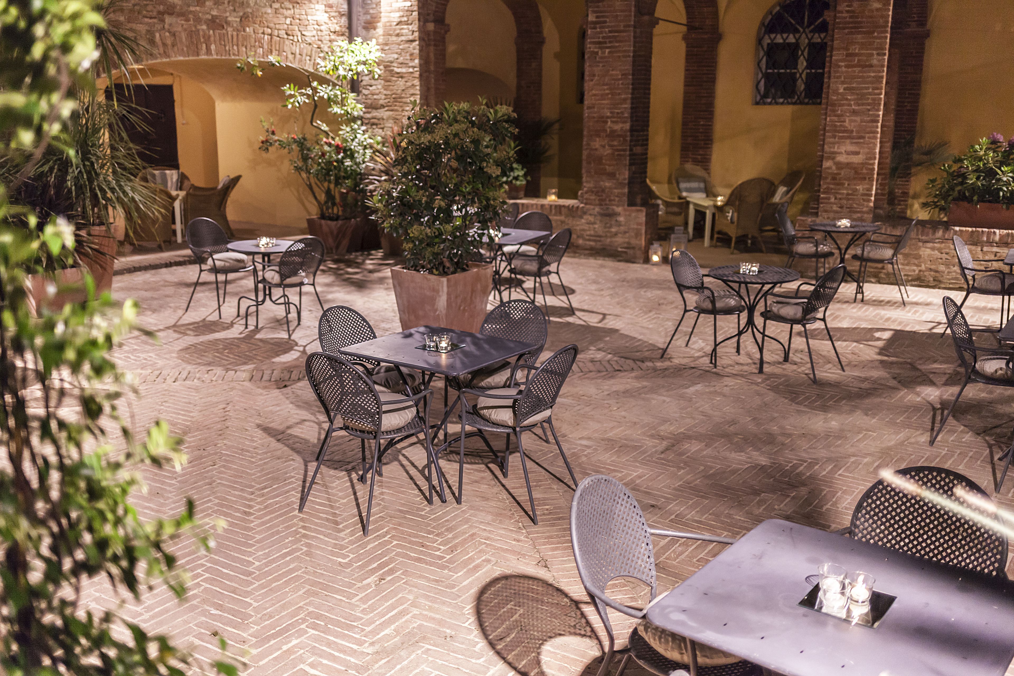 Un patio al aire libre con mesas y sillas, rodeado de muros de ladrillo y plantas en macetas.