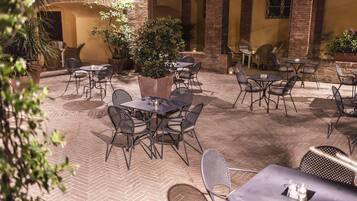 Un patio al aire libre con mesas y sillas, rodeado de muros de ladrillo y plantas en macetas.