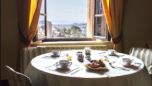 Una mesa de comedor con tazas, platos y un croissant, frente a una ventana con cortinas.