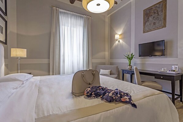 Habitación de hotel con cama, escritorio, televisión, ventana con cortinas y una planta.