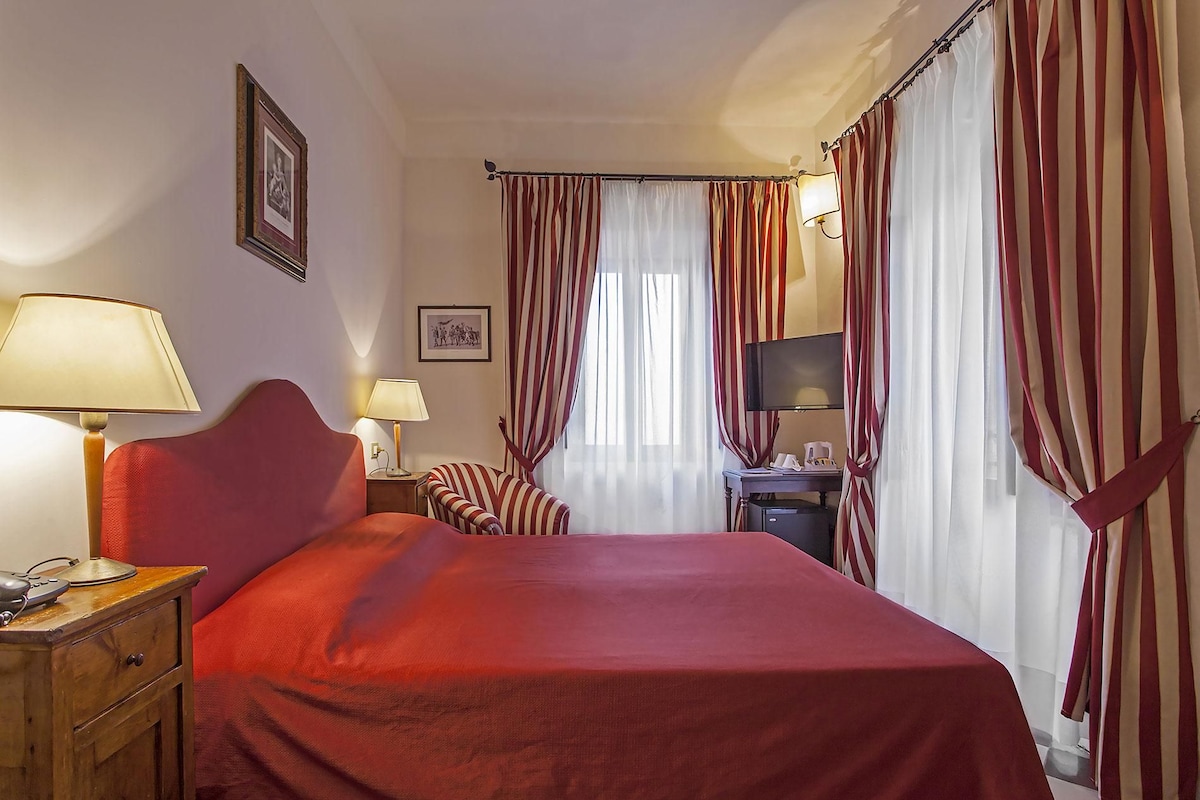 A hotel room with a large bed, two bedside tables, a desk with a chair, a television, and striped curtains.