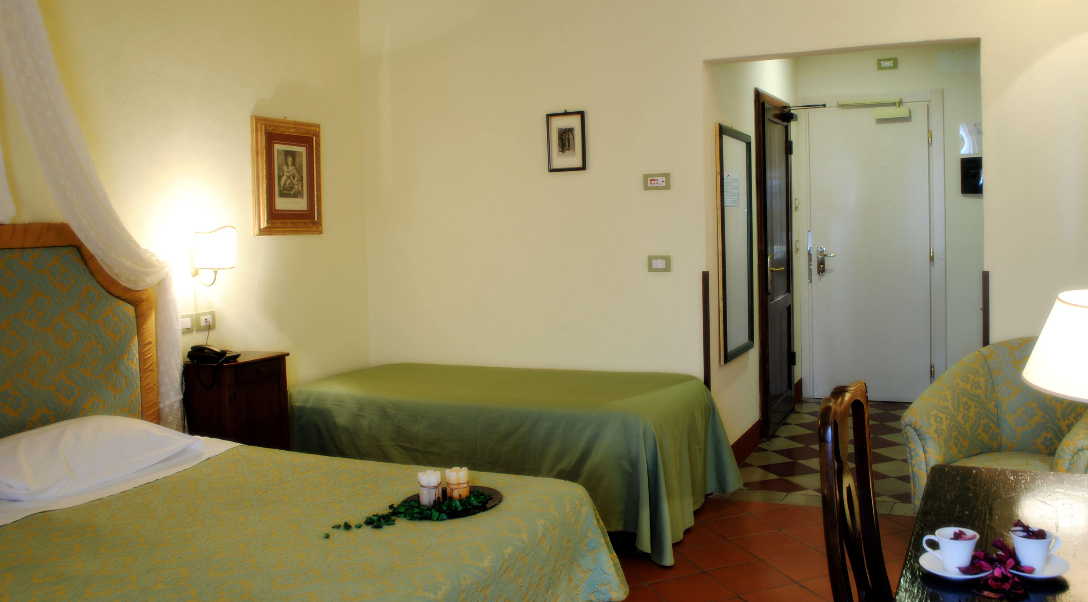 Une chambre d’hôtel avec deux lits, une petite table avec des bougies, une chaise et une porte donnant sur une autre pièce.