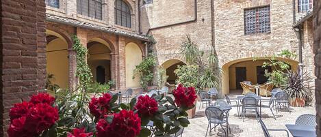 A courtyard with brick buildings, outdoor seating, and potted plants.