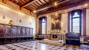 Interior de iglesia con bancas de madera, un altar de madera y un cuadro grande en la pared.