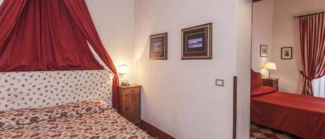A bedroom with a canopy bed, two bedside tables with lamps, a checkered floor, and a mirror reflecting the room.