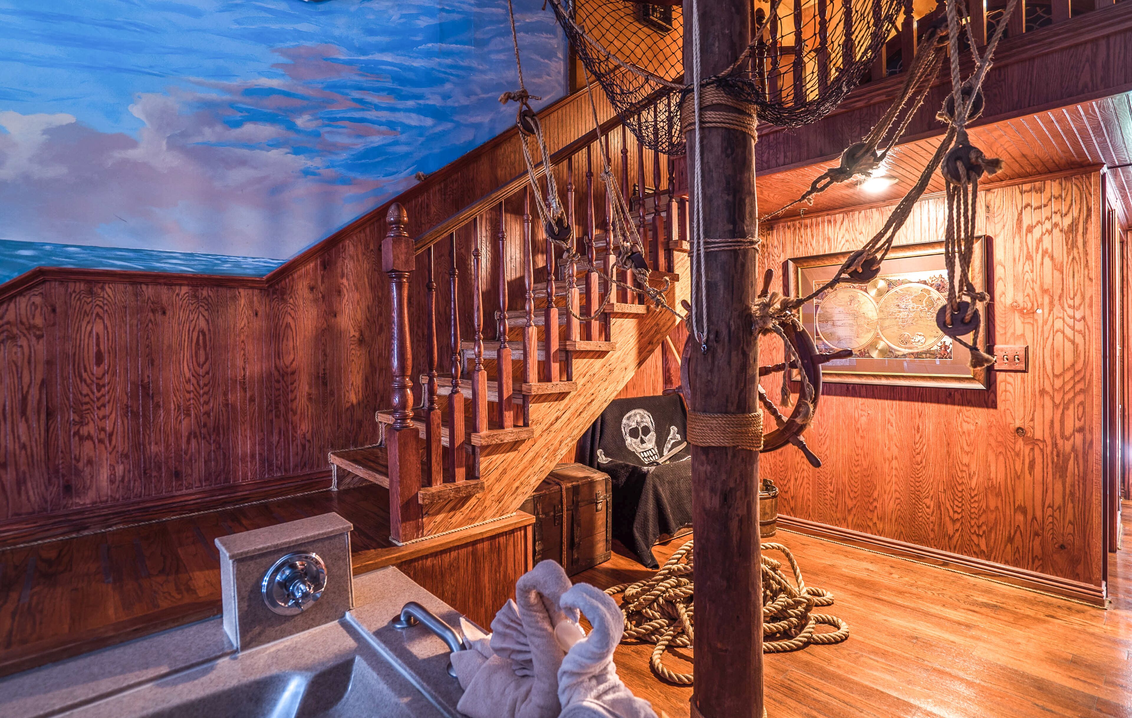 A wooden staircase with a rope and skull decoration, a ship's wheel, and a nautical-themed room.
