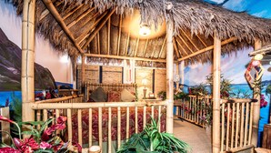 A room with a thatched roof, bamboo furniture, and tropical plants. - Anniversary Inn - 5th South (Salt Lake City)