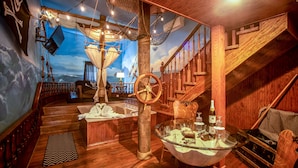 A nautical-themed room with a wooden staircase, a ship's wheel, and a mural of the ocean. - Anniversary Inn - 5th South (Salt Lake City)