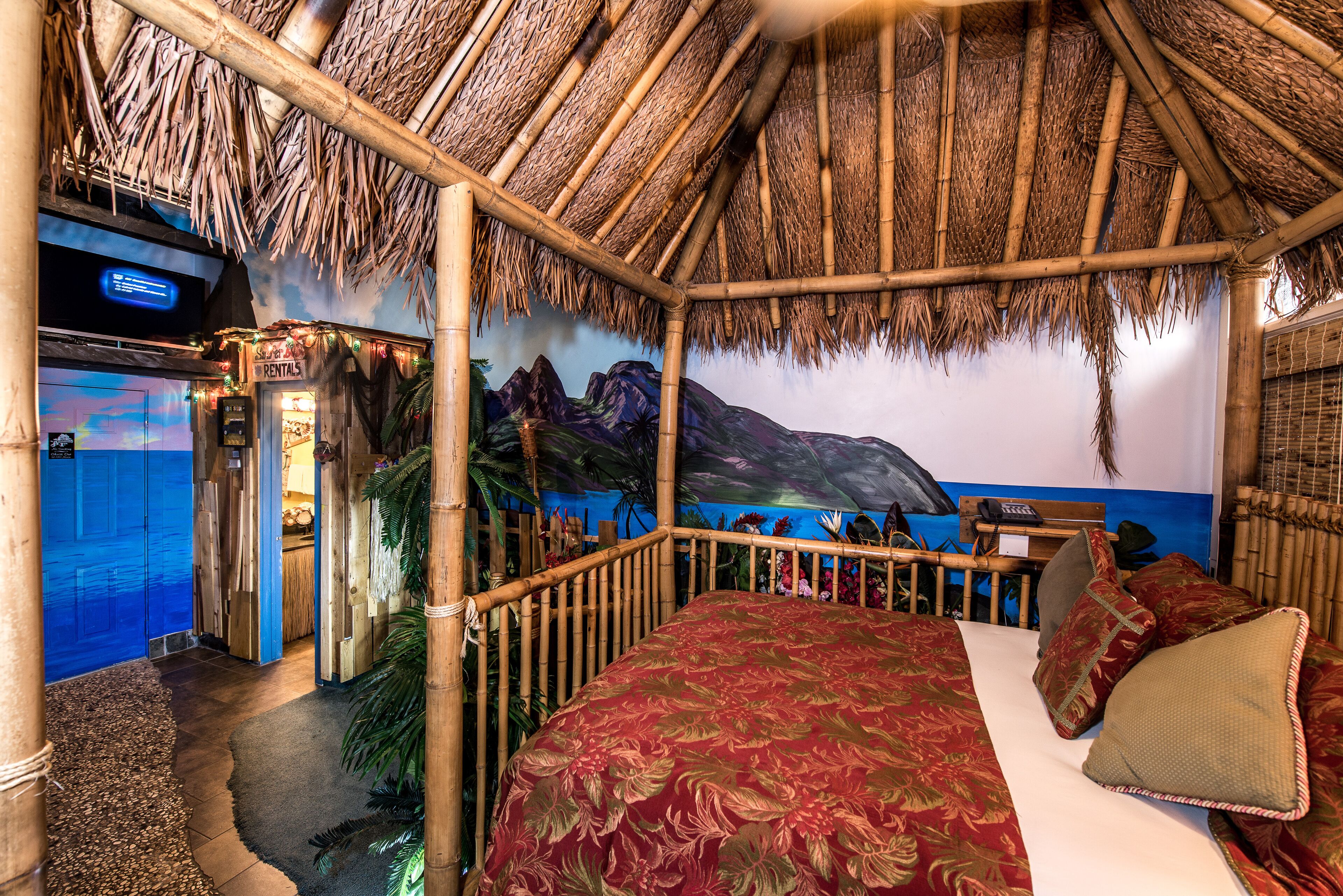 A room with a bed, a bamboo ceiling, a mural of a mountain, and a rental sign.