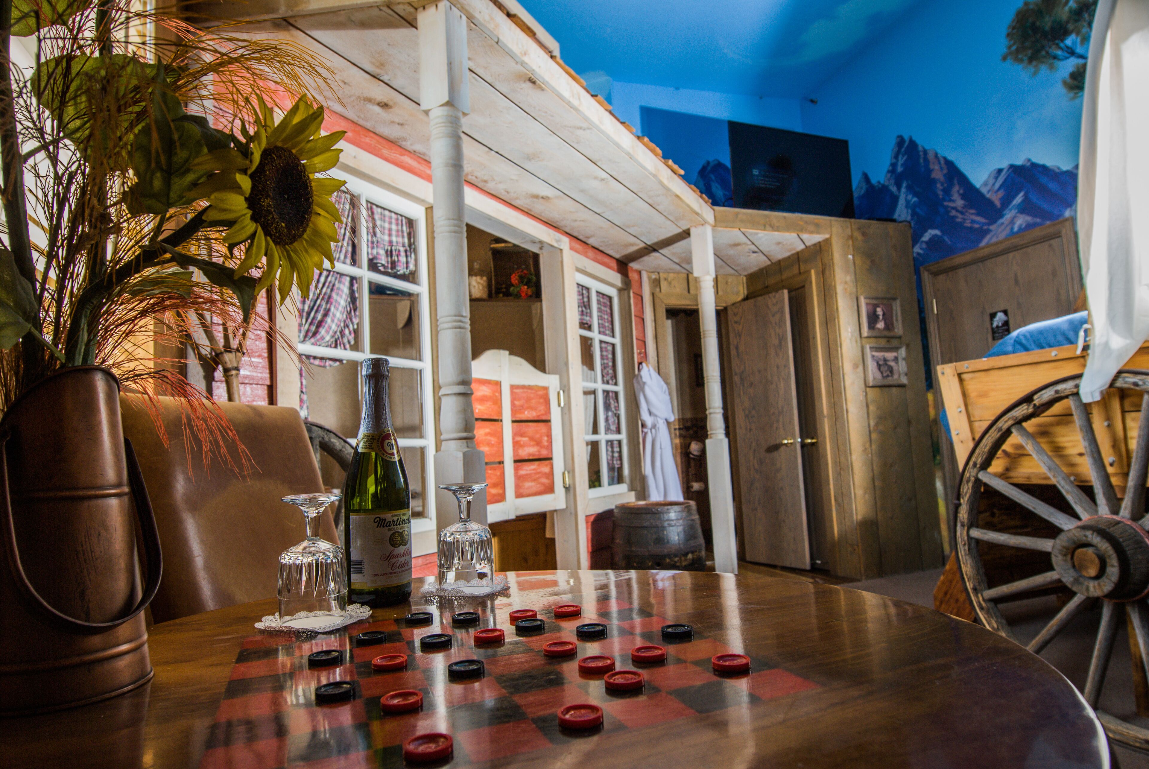 A checkered board game with bottle caps, a vase with dried plants, and a rustic wooden table in a room with a mountain mural.