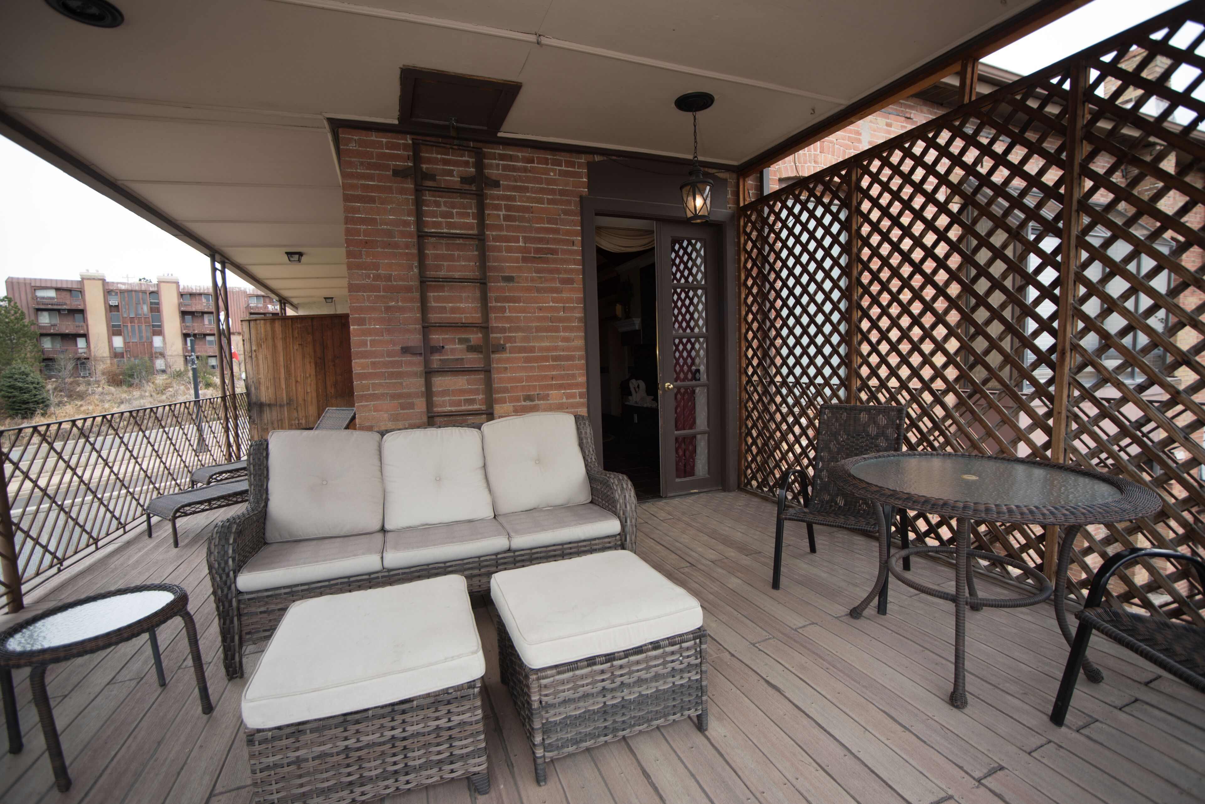 A covered outdoor patio with wicker furniture, a table, and a view of the cityscape.