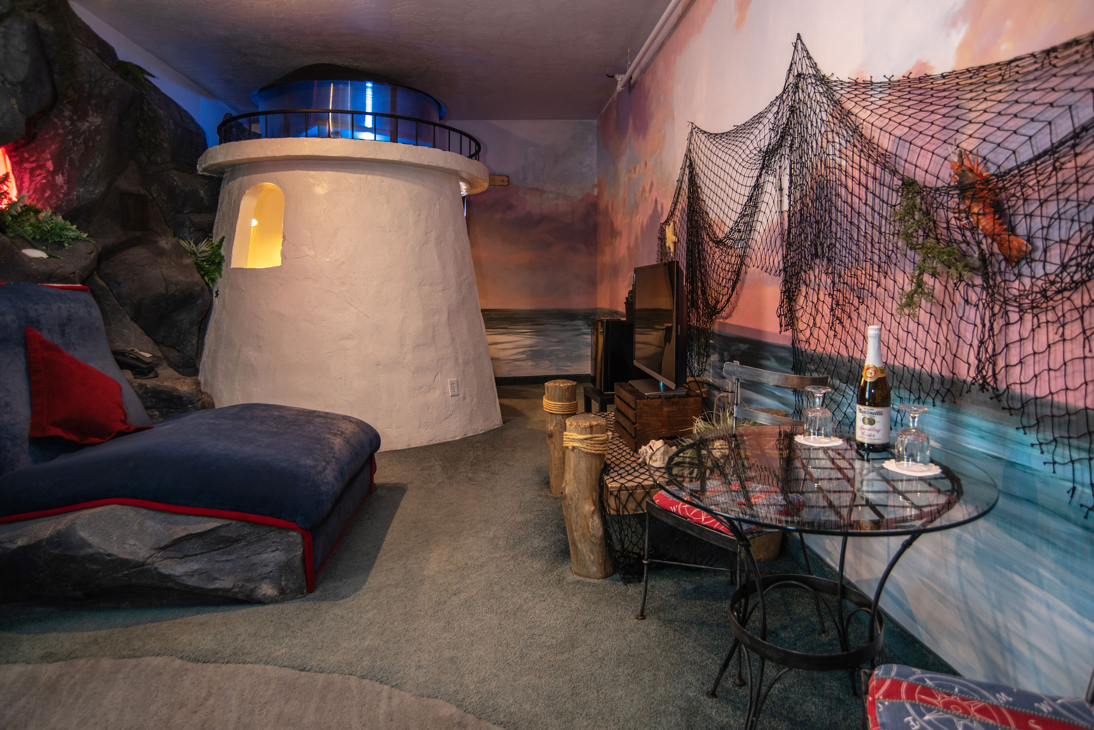 A cozy room with a round table set for two, a comfortable sofa, a decorative wall mural, and a unique lighthouse-like structure.