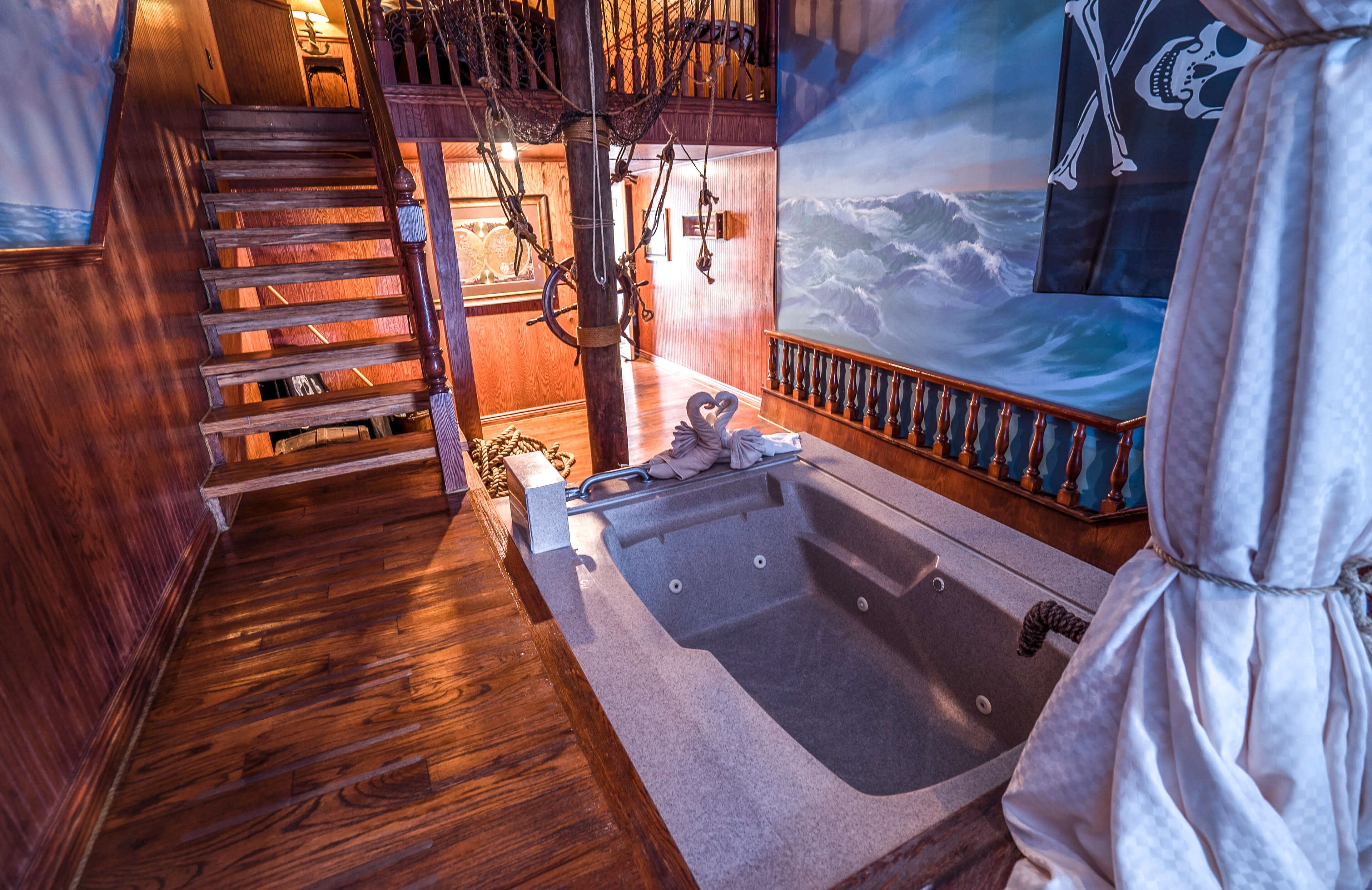 A wooden staircase leading to a room with a large bathtub, nautical-themed decorations, and a mural of the ocean.