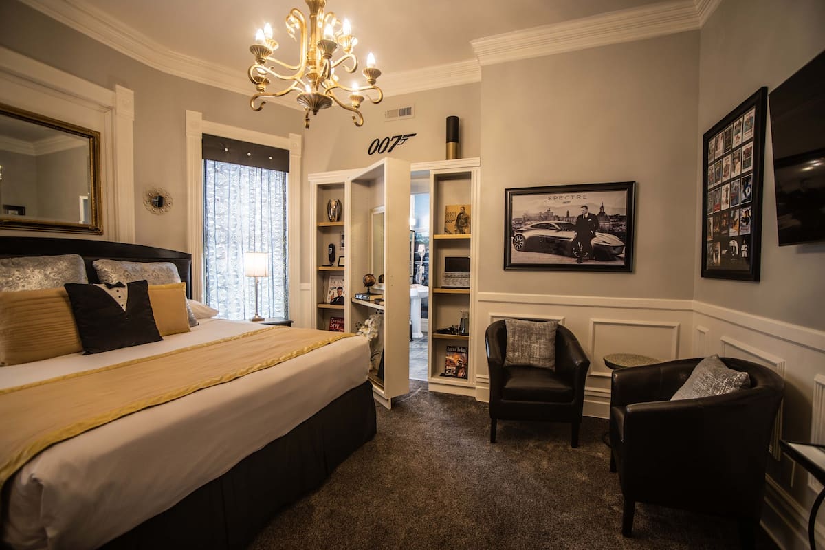 A bedroom with a large bed, a chandelier, a wardrobe, a chair, and a television.