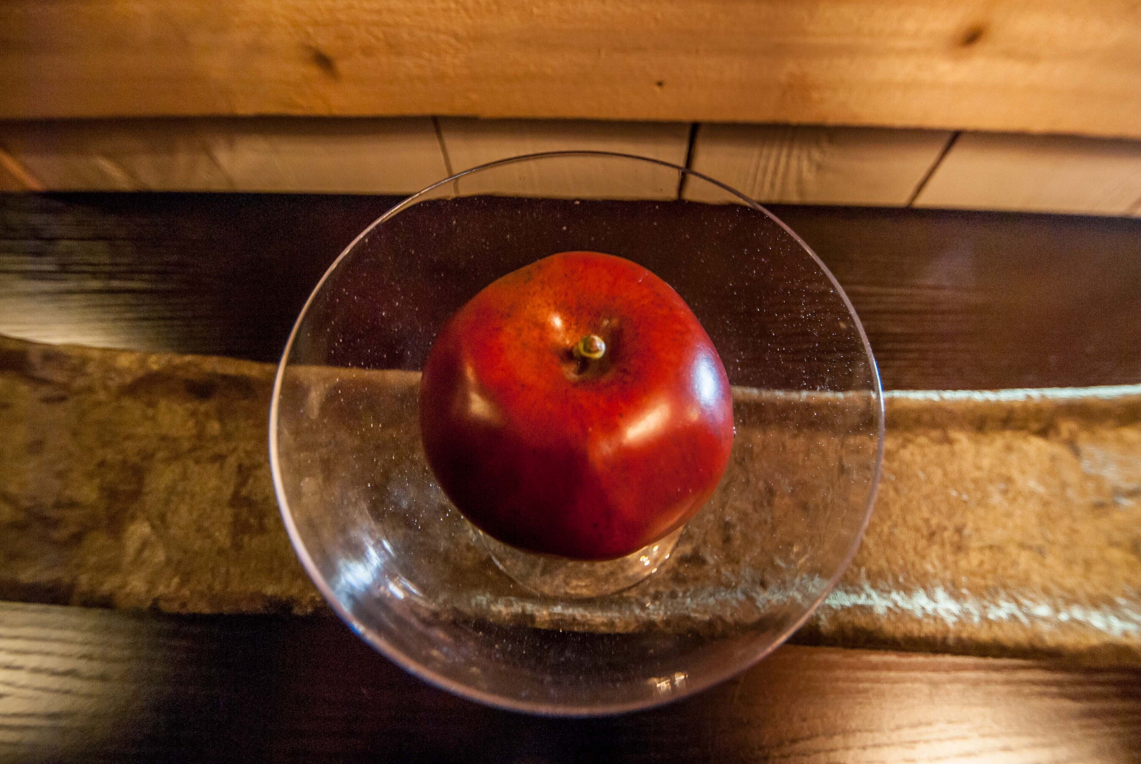 Une pomme rouge dans un saladier en verre transparent, posée sur une surface en bois.