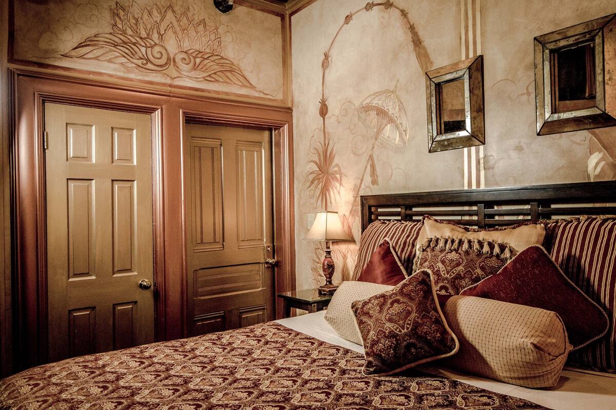 A hotel room with a large bed, ornate ceiling, and a wooden door.