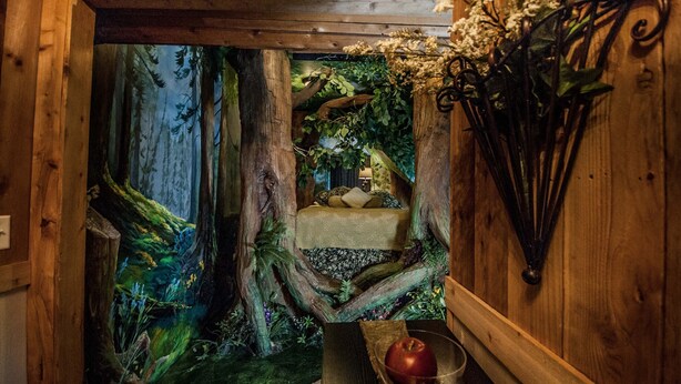 Habitación acogedora con una cama centrada bajo una viga de madera, rodeada por un mural con motivos forestales.