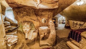 Una habitación con una gran escultura de cabeza de piedra, una bañera y una cama con colcha estampada.