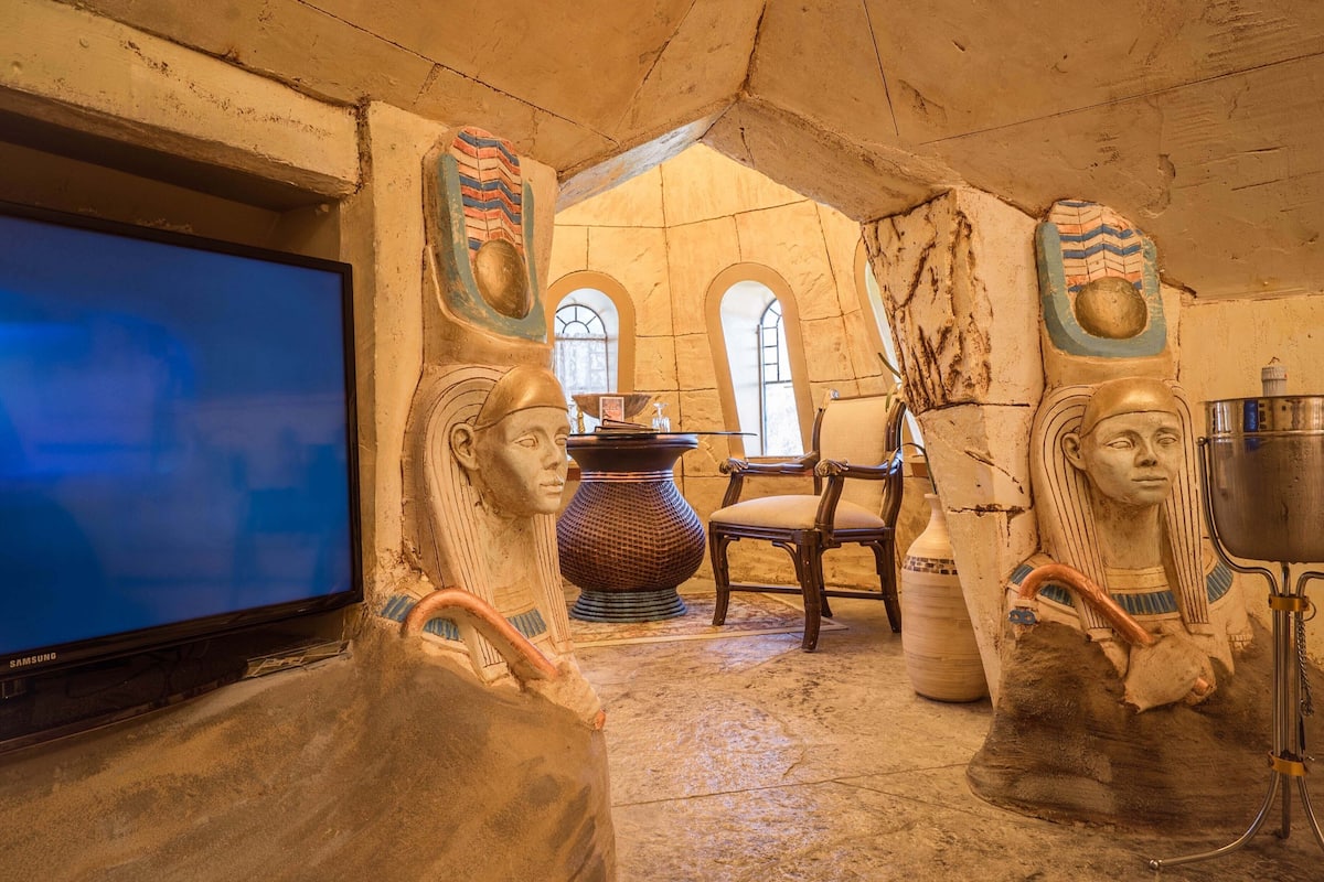 A room with a television, Egyptian-themed decor, a chair, and a large vase.