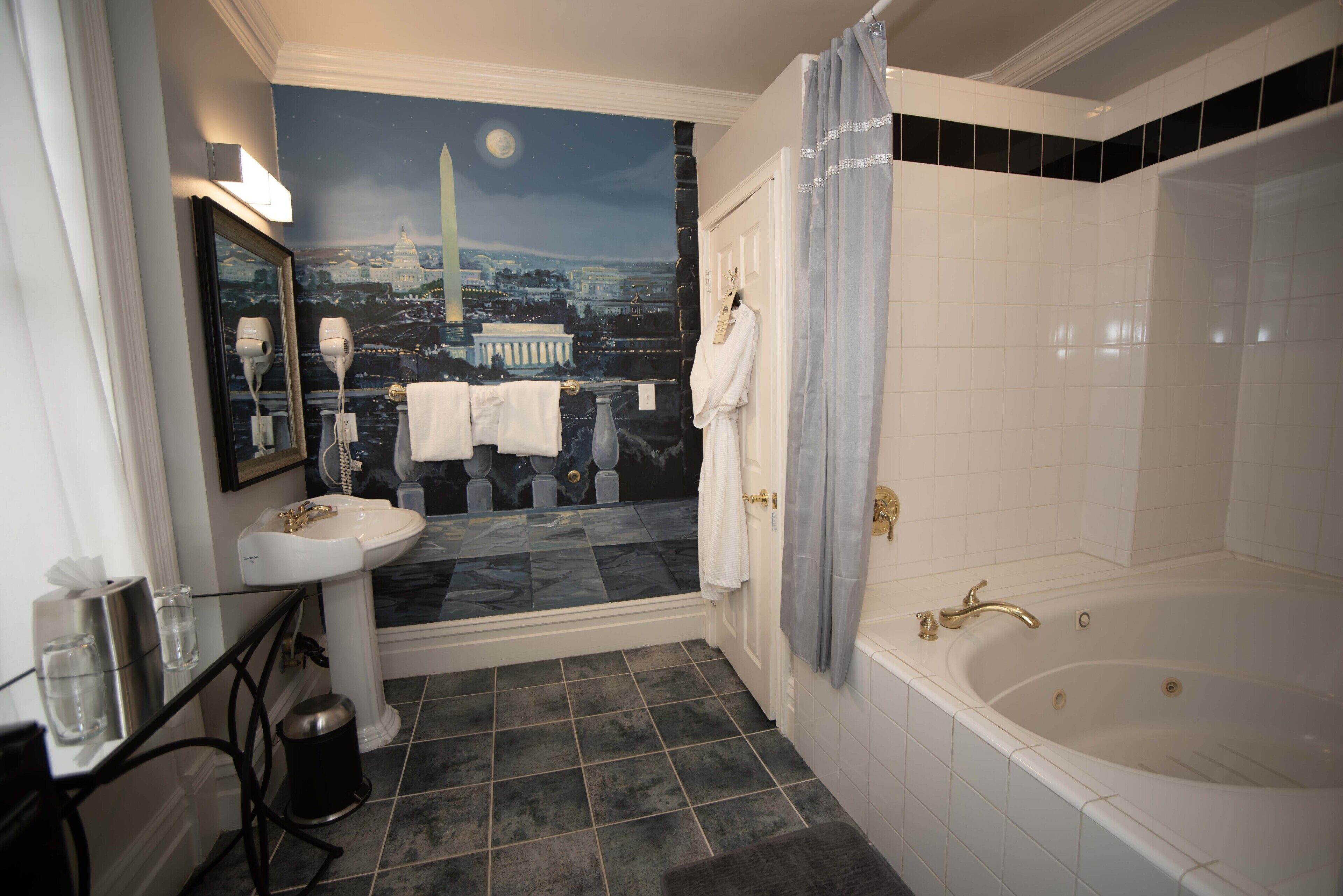 A bathroom with a large bathtub, a sink, a mirror, and a wall mural depicting a cityscape at night.