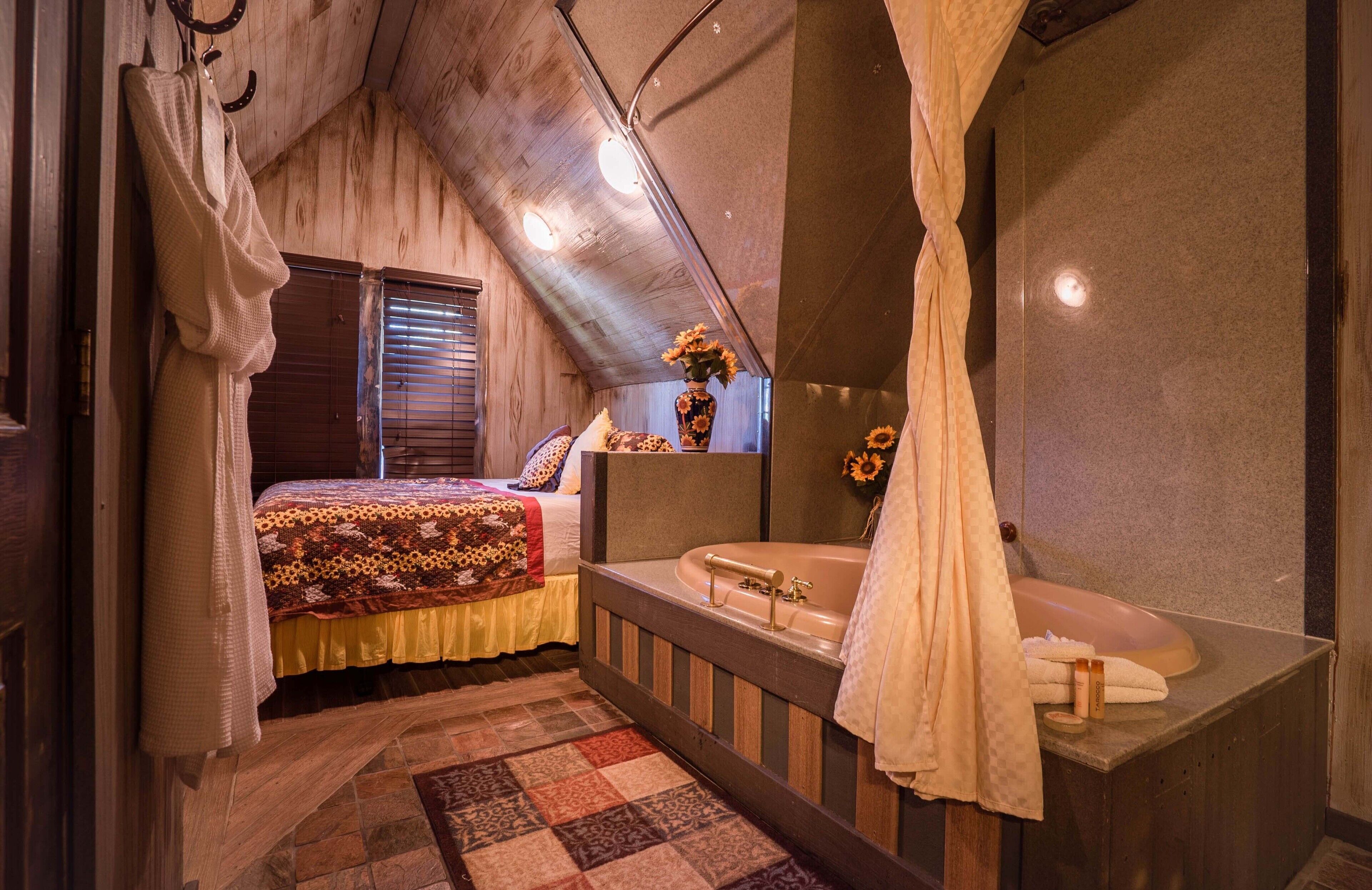 Ein Schlafzimmer mit Bett, großem Fenster, Schminktisch mit Spiegel und Badewanne.