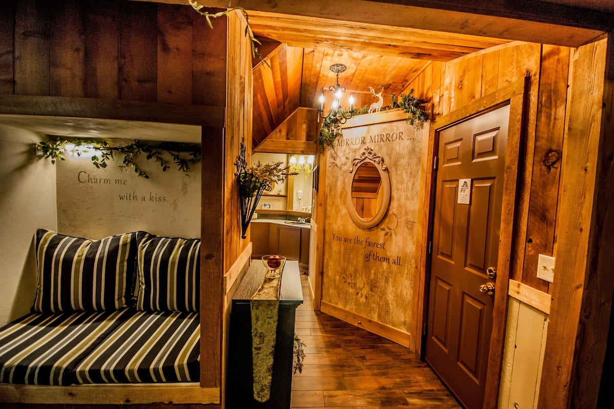 A wooden interior with a bench, a mirror with a decorative frame, and a door with a sign.