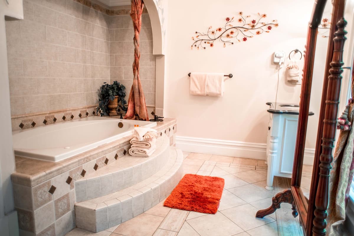 A bathroom with a large bathtub, a wooden chair, a red rug, and a decorative wall piece.