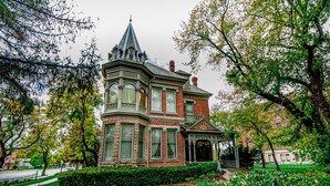 Un edificio de estilo victoriano con una torre destacada, rodeado de jardines cuidados y un camino pavimentado.