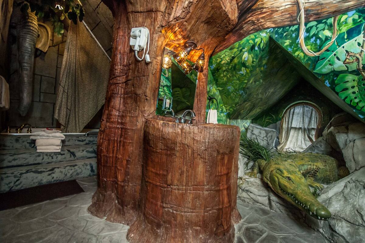 A bathroom with a tree trunk sink, a crocodile decoration, and a mirror with a hanging light fixture.