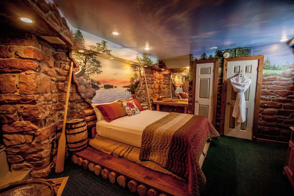 A room with a stone wall, wooden bed, and a mural of a sunset.