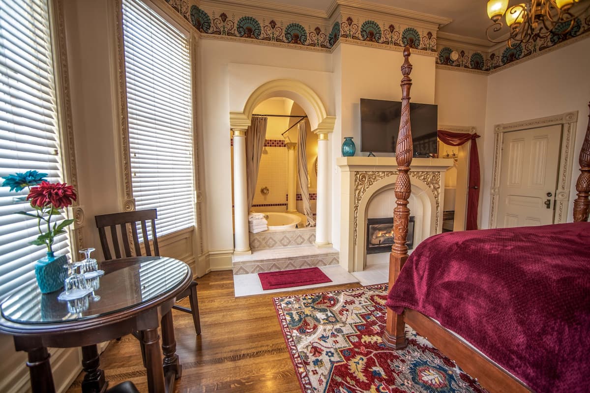 A bedroom with a four-poster bed, a fireplace, and a TV mounted above it.