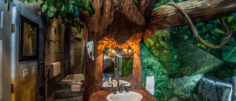 A bathroom with a sink set in a tree stump, surrounded by lush greenery and a mirror.