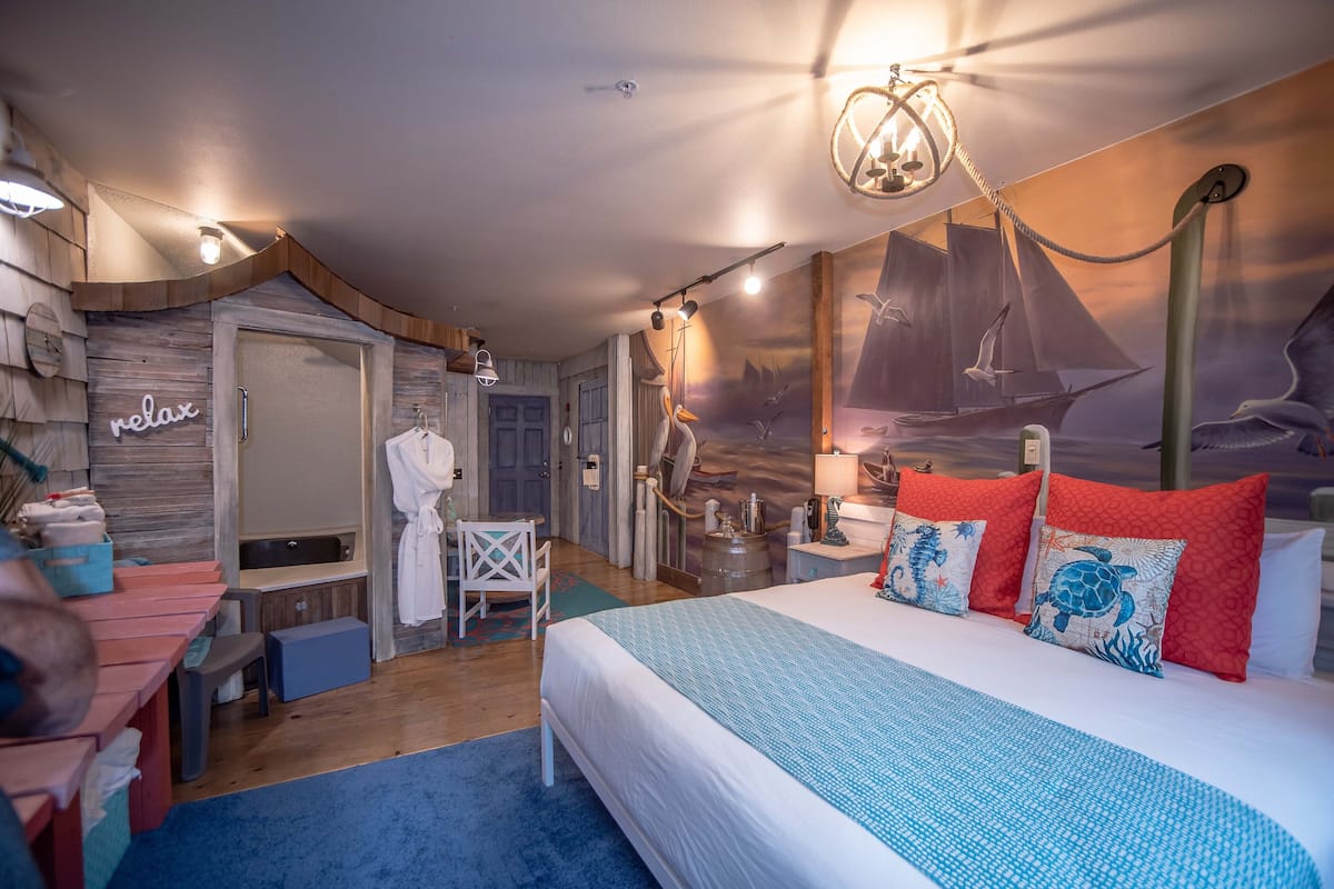 Une chambre avec un grand lit, une tête de lit en bois, une fresque représentant un voilier et un panneau « détendez-vous » accroché au mur.