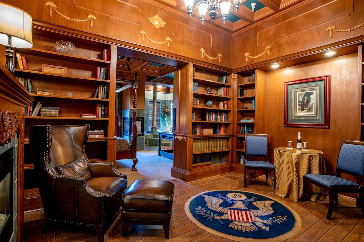 Une bibliothèque avec des étagères en bois, des fauteuils en cuir et un tapis rond orné d’un motif d’aigle.