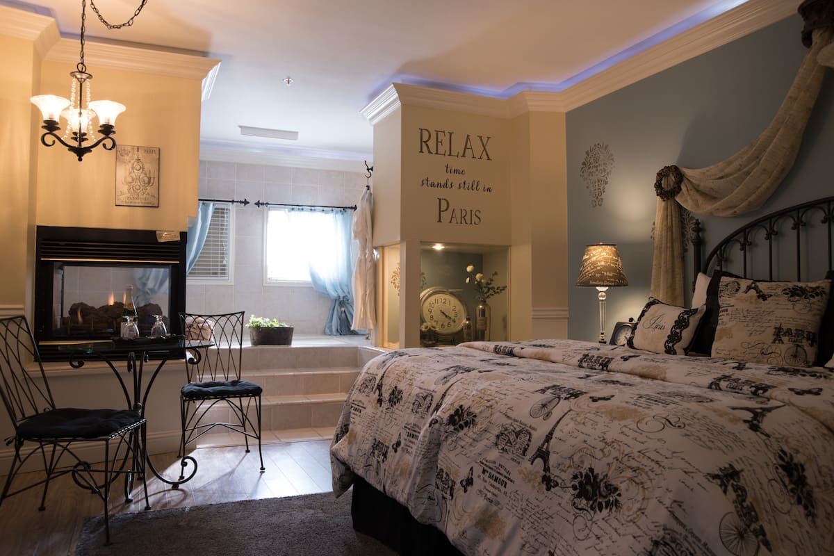 Une chambre avec un lit, un bureau avec des chaises, une cheminée et un mur orné d’une inscription : « À Paris, le temps s’arrête, profitez-en. »