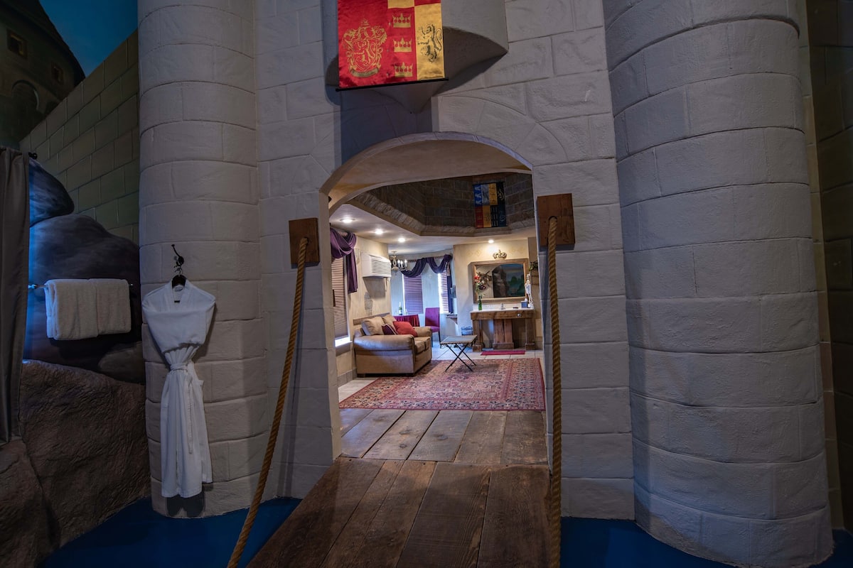 Une pièce à thème médiéval avec des murs en pierre, un plancher en bois et un coin salon confortable avec un canapé et une petite table.