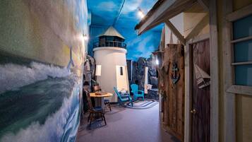 A room with a mural of a lighthouse, a round table with chairs, and a wooden door.