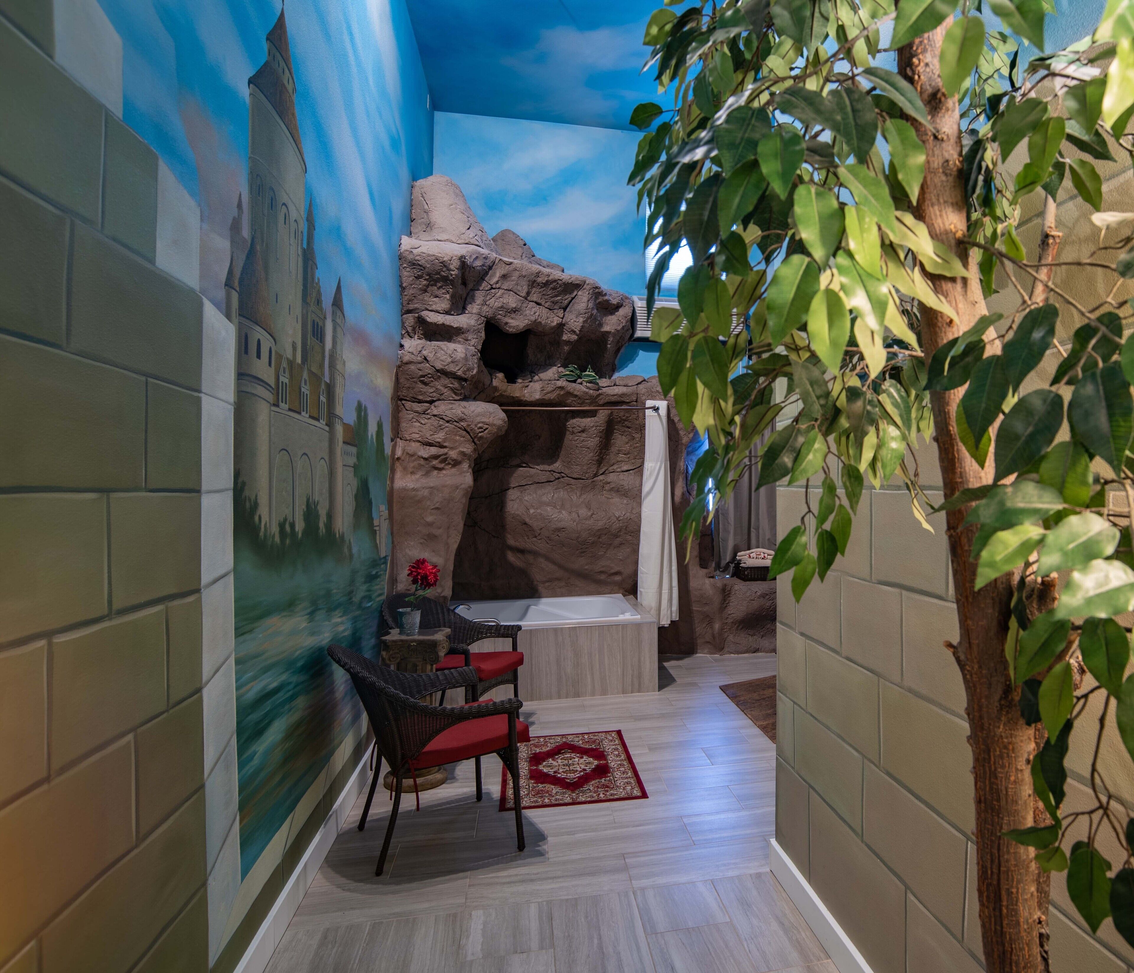 Un couloir étroit, avec une fresque représentant un château sur le mur de gauche, une formation rocheuse sur le mur de droite, une petite table avec une chaise et une plante.