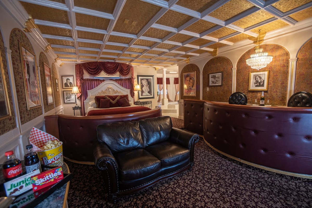 Une chambre d’hôtel avec un grand lit, un canapé en cuir, un comptoir d’accueil aux lignes courbes et un lustre.