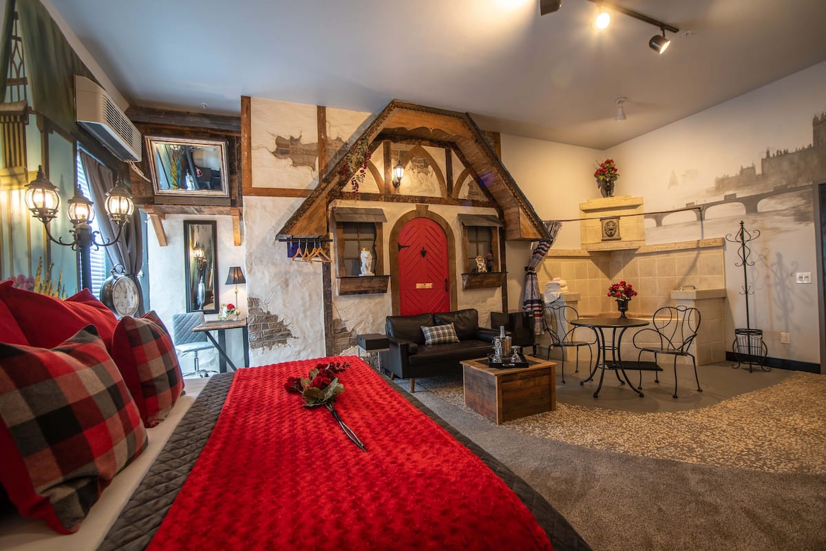 Une pièce confortable avec un lit, une porte rouge, une cheminée, un coin repas et un miroir.