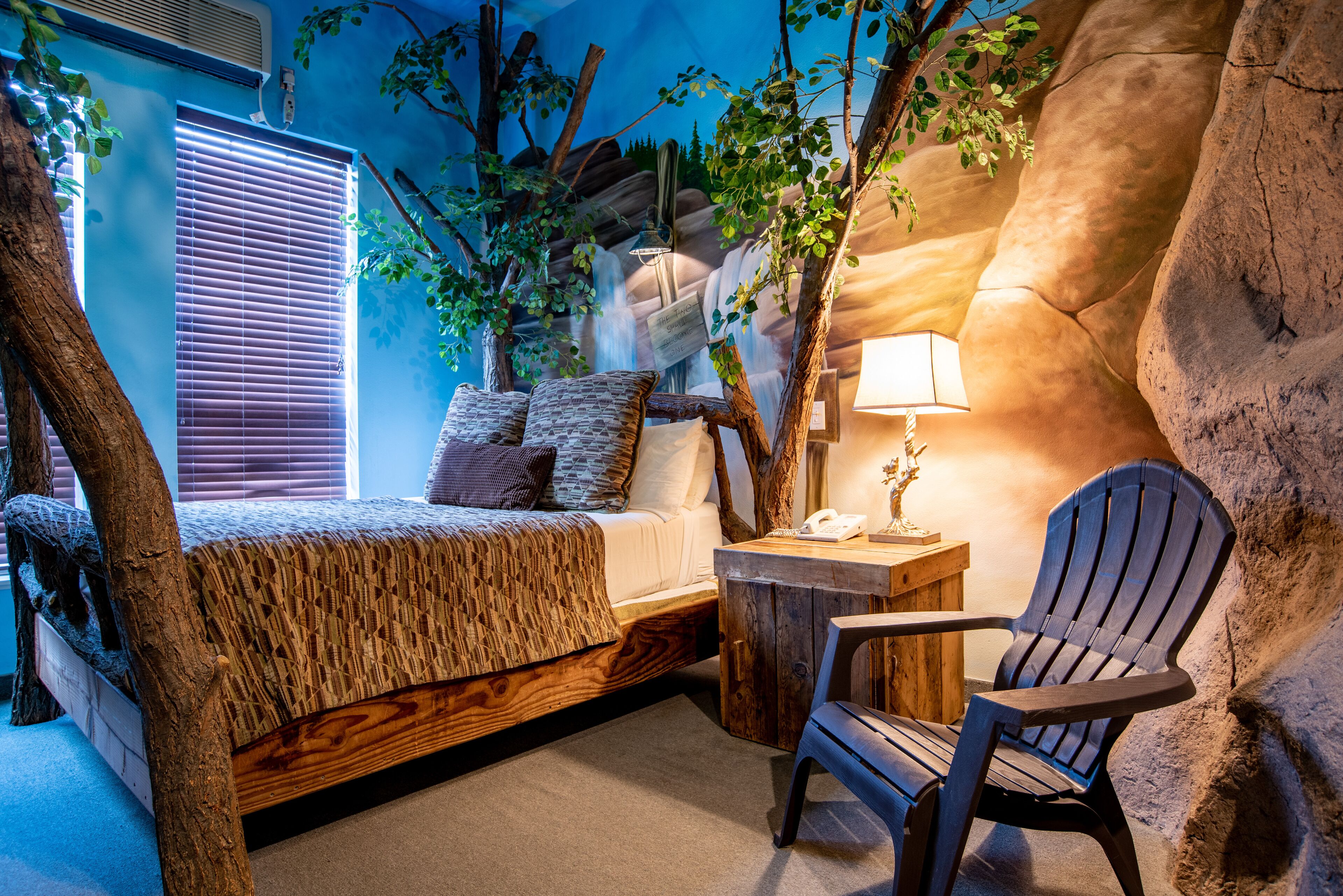 Une chambre avec un lit décoré sur le thème des arbres, un bureau avec une lampe et une chaise.