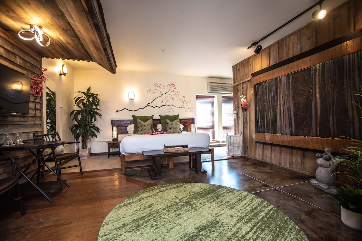 Une pièce comprenant un lit, une table à manger, des chaises, un tapis vert et un mur en bois.